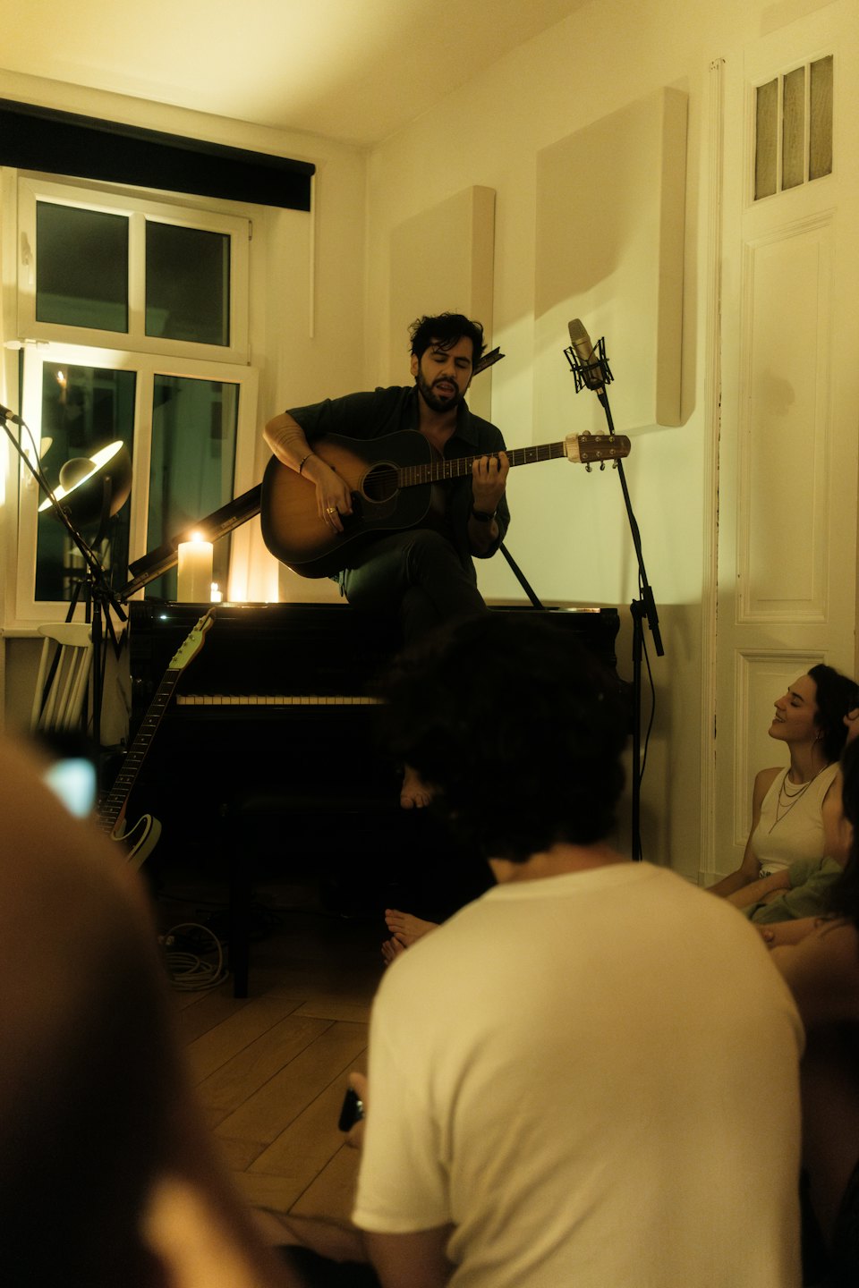 Bearded man plays guitar and sings into a microphone at a concert.